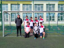 Drużyna piłkarzy z Młodojewa składająca się z 7 chłopców ubranych w biało-czerwone koszulki. Na zdjęciu znajduje się również nauczyciel wychowania fizycznego. Drużyna stoi na tle bramki na boisku orlik.